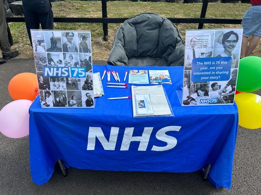 Picture of table with NHS table cloth on it also has information and balloons on it