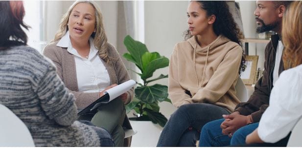 5 people sat in a circle having a discussion with one holding a clipboard