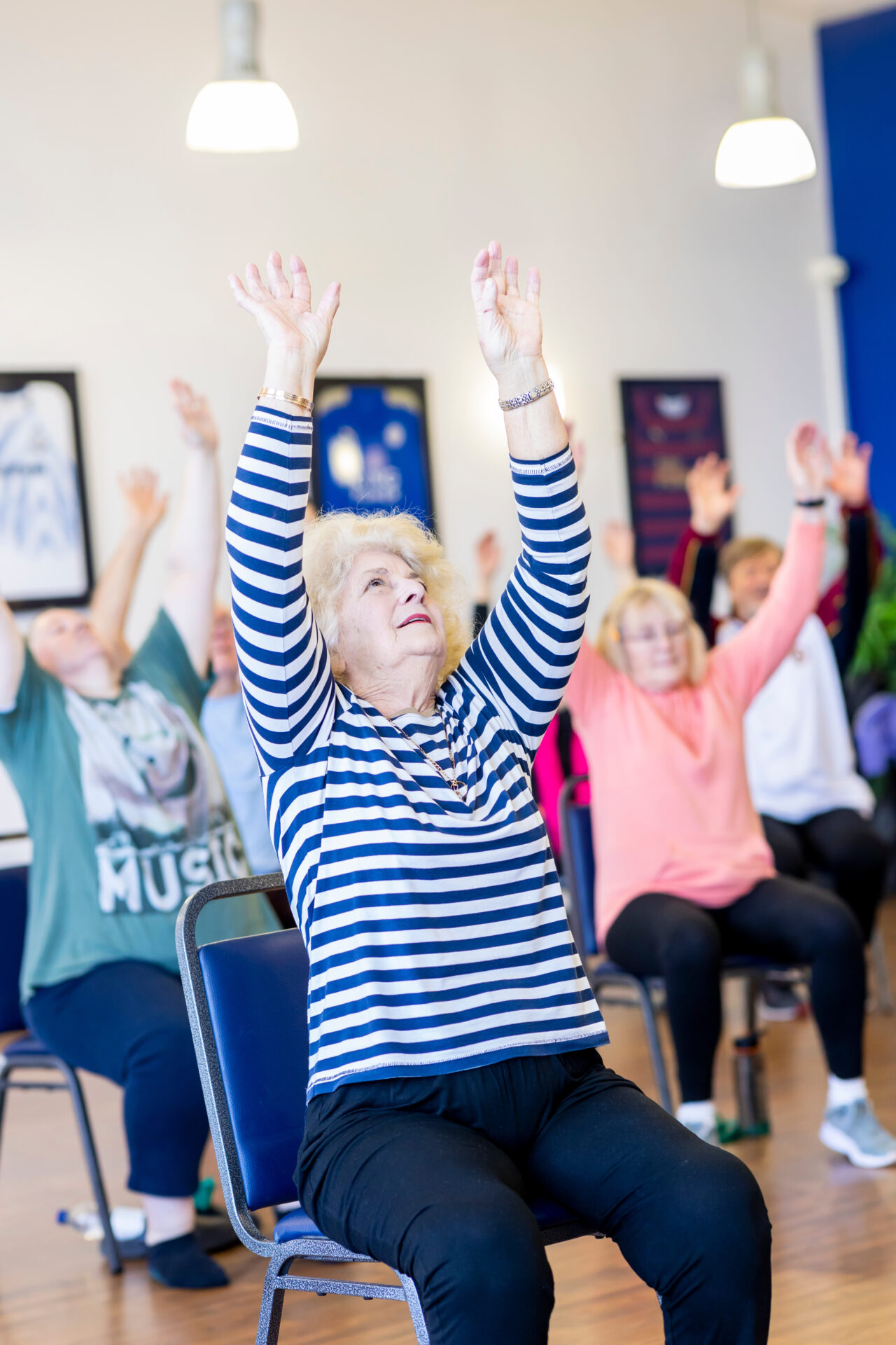 Picture of people sat on chairs exercising with arms outstretched above head