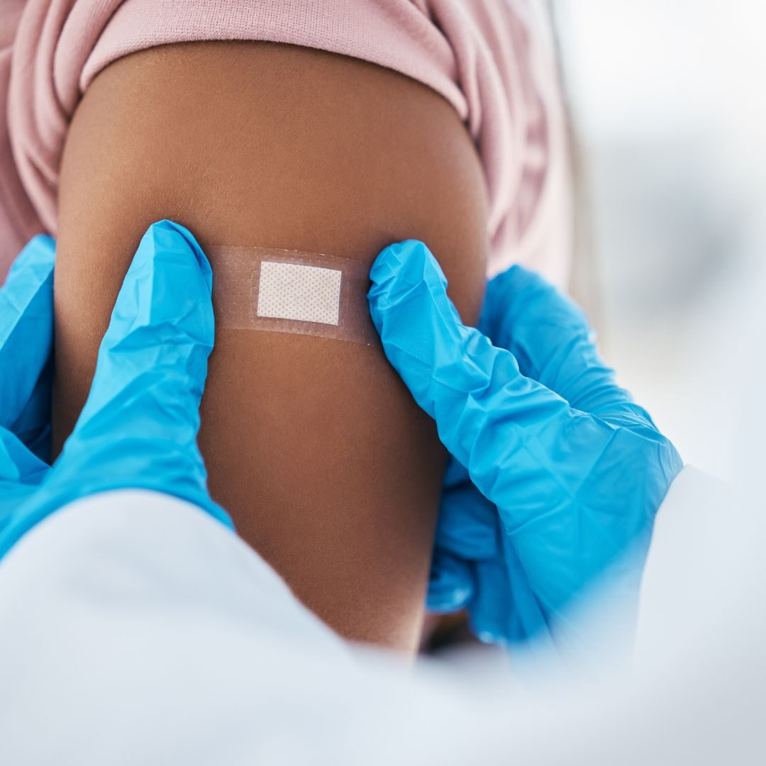 A photograph of someone in blue gloves putting a plaster over an arm.