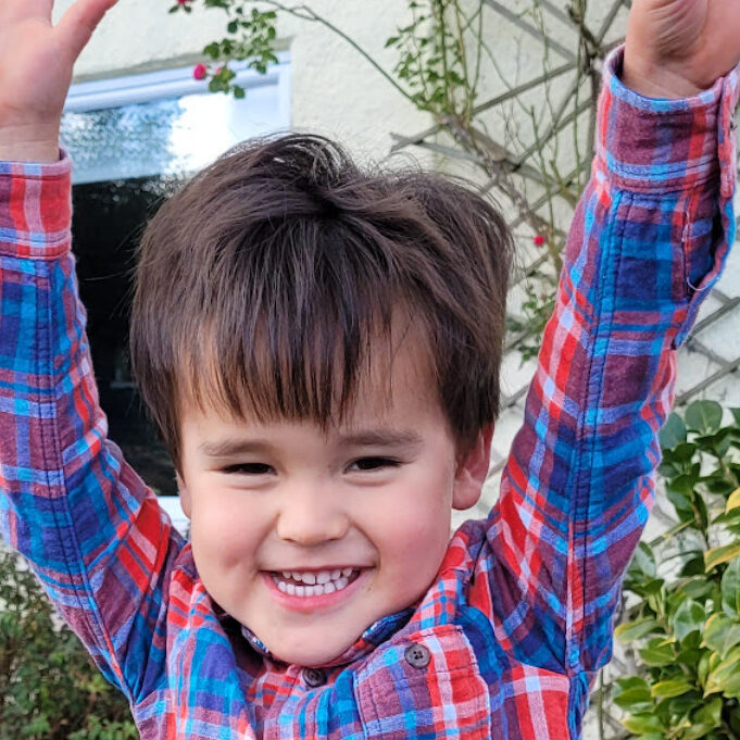 Picture of a young child stood outside holding up his arms above his head and smiling