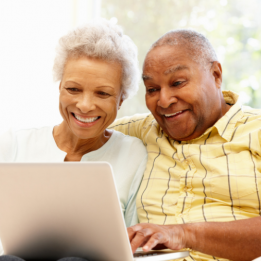 Picture of two people sat looking at a laptop screen and smiling