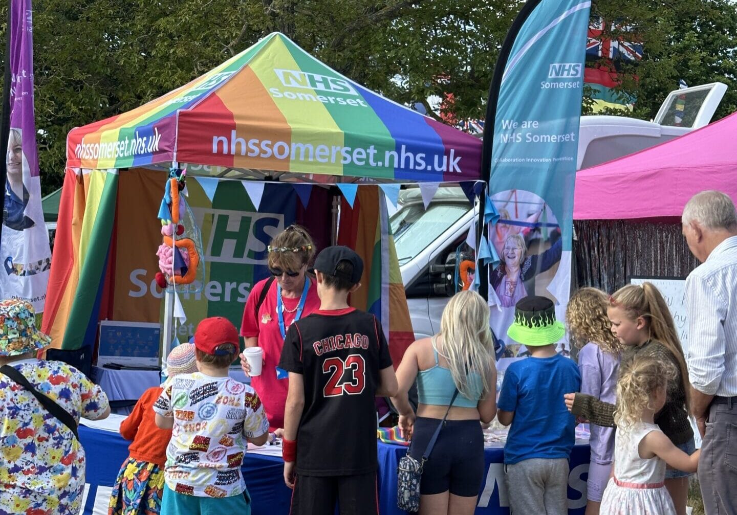 Photo 08-06-2024, 16 58 35 Picture of NHS Somerset's rainbow gazebo at an event with people wandering around.