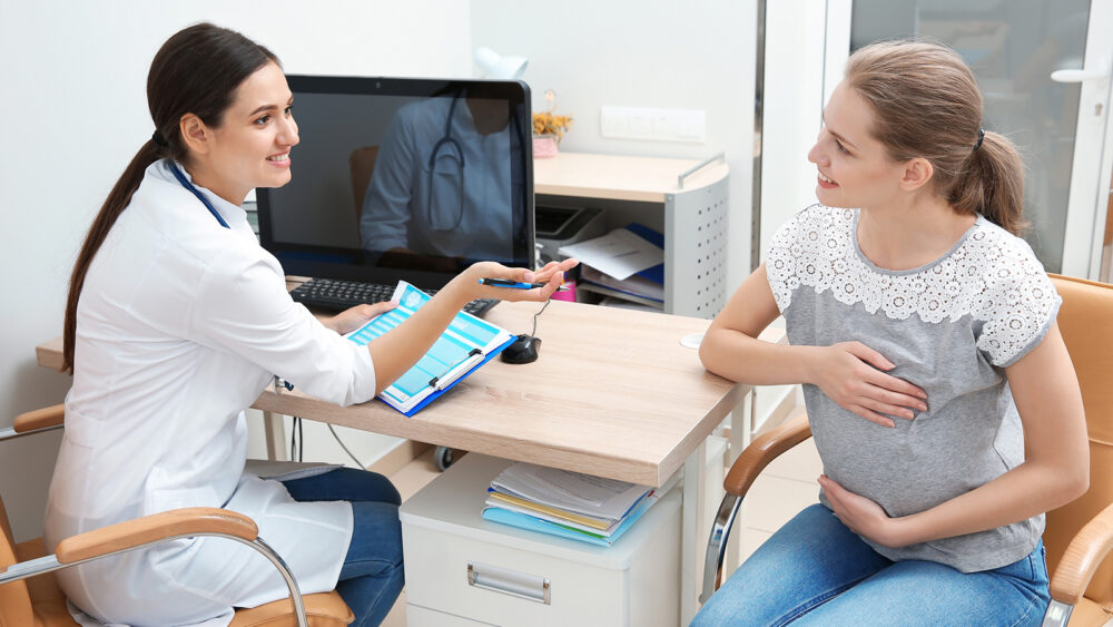 A female GP speaking with a pregnant woman and holding a medical document, both are smiling.